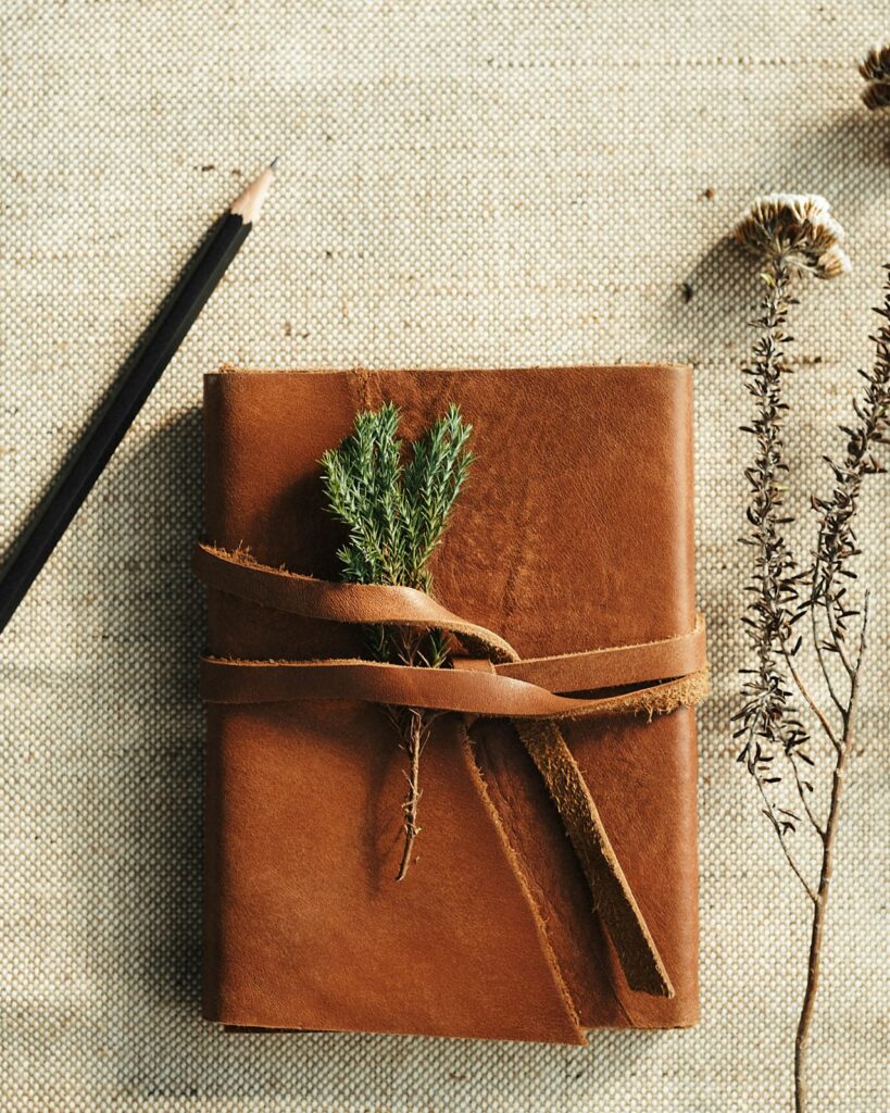 Leather-bound journal tied with a strap, beside a pencil and dried flowers on linen
