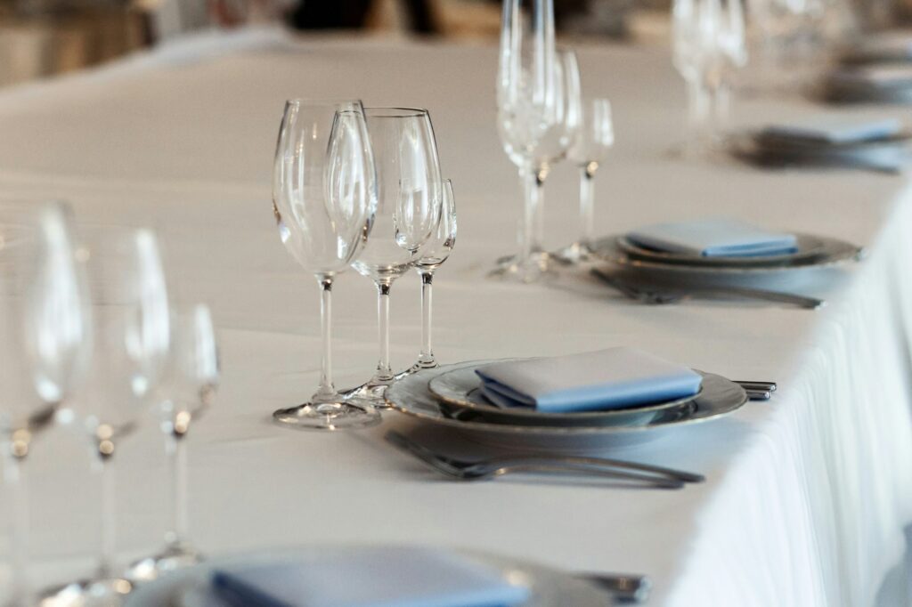 Long banquet table set with wine glasses, white plates and folded blue napkins