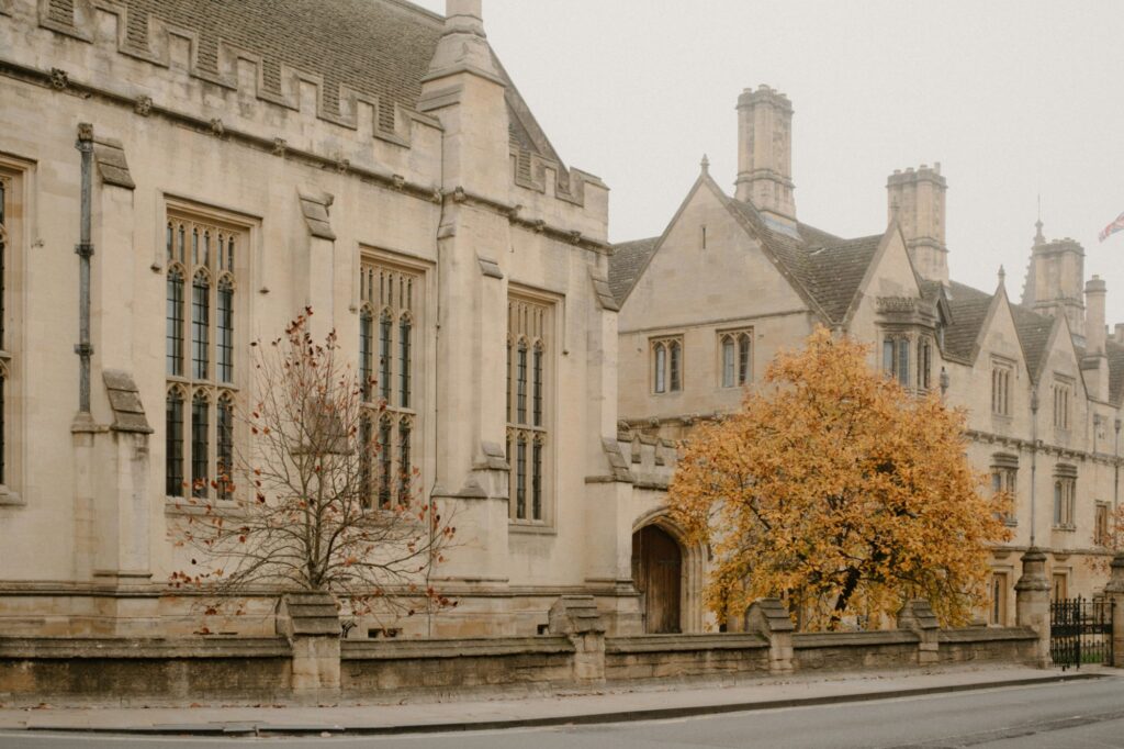 Stone school building with tall windows behind a tree in autumn color