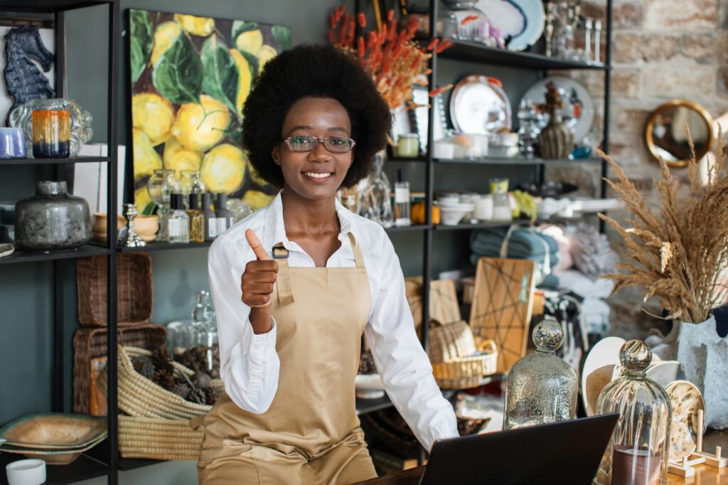 Shop owner smiling at the counter of a store stocked with ceramics, plants and gifts