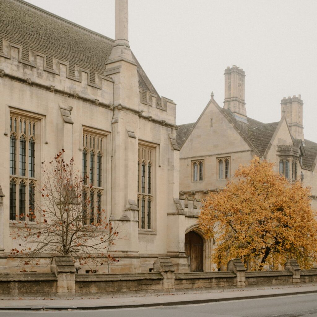 Stone school building with tall windows behind a tree in autumn color